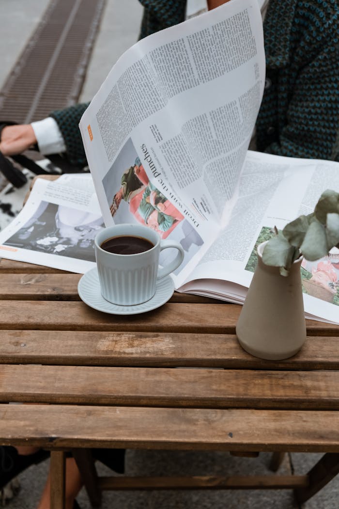 A relaxing moment at an outdoor café with coffee and a newspaper on a wooden table.
